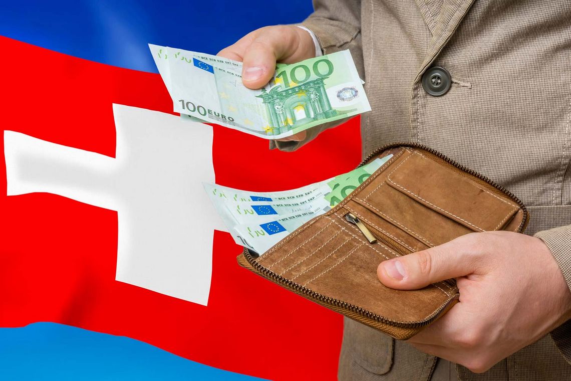 Foto von einer Person, die Geldscheine aus der Geldbörse zieht; im Hintergrund ist die Schweiz-Flagge